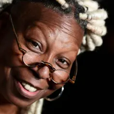 Uśmiechnięta Whoopi Goldberg w okularach i z dredami. Ikona kina, znana z wielu filmów, seriali i programów.