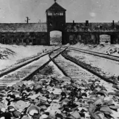 Brama obozu koncentracyjnego Auschwitz-Birkenau zimową porą. Tysiące porzuconych przedmiotów, świadectwo okrucieństw minionych epoki, leży przy torach kolejowych.