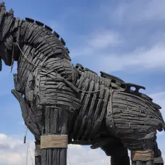 Gigantyczny, drewniany koń trojański, symbol podstępu i legendy, stoi na tle błękitnego nieba z chmurami.