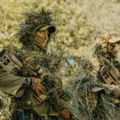 Dwóch snajperów w ghillie suit, ukrytych w zaroślach, czeka na cel.