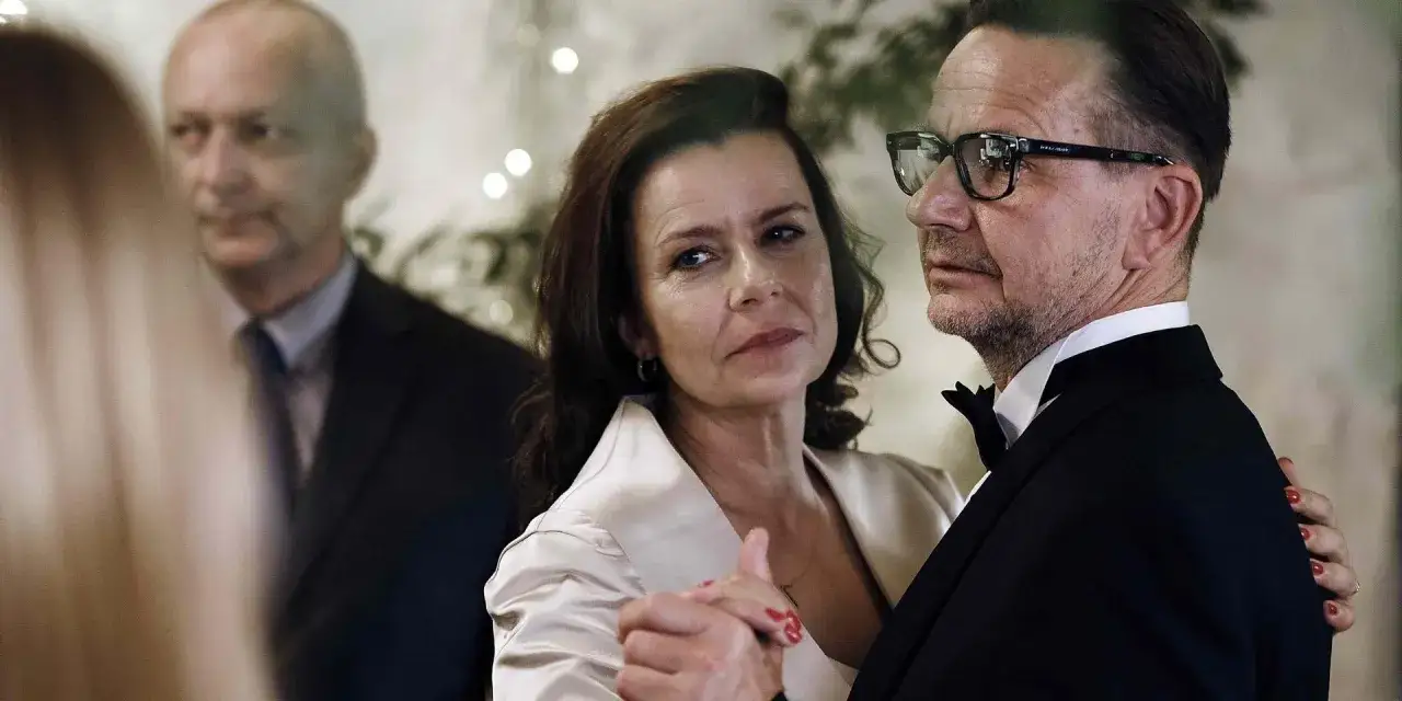 Agata Kulesza w eleganckiej kreacji tańczy z partnerem. W tle widać innych uczestników przyjęcia.