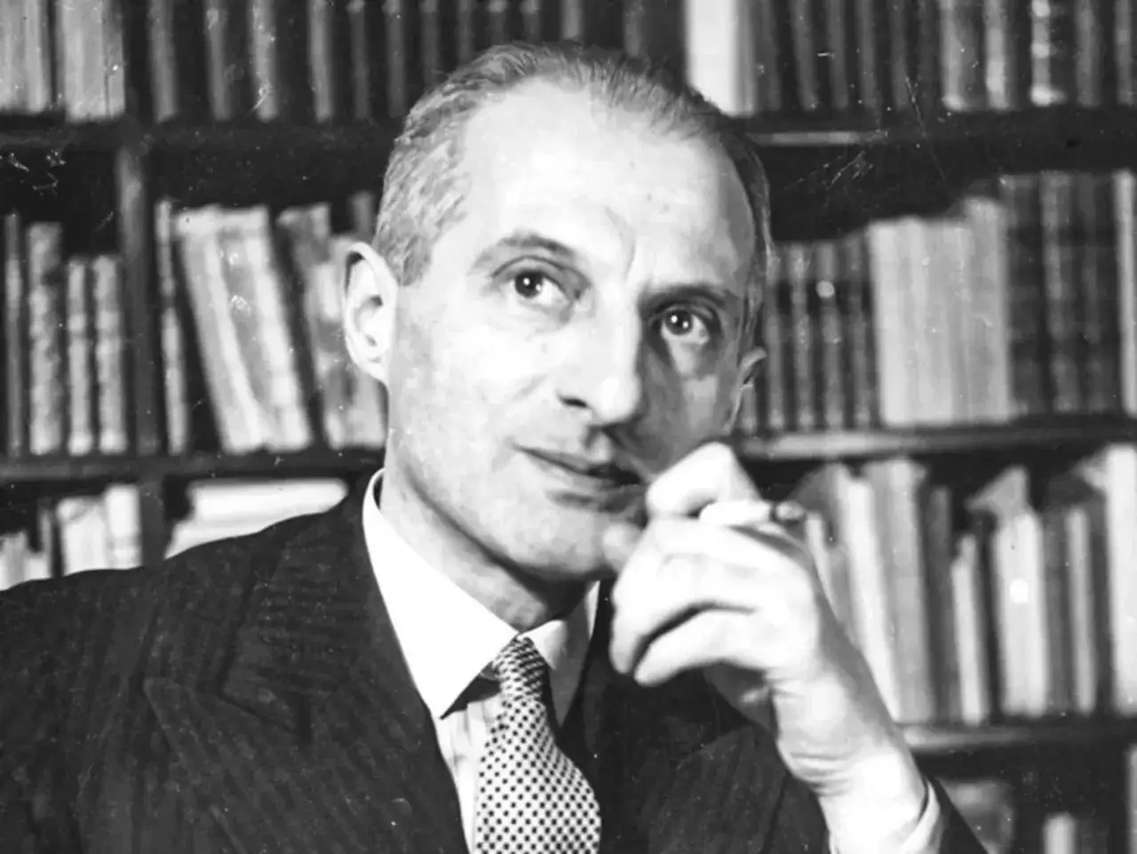 Julian Tuwim z papierosem w dłoni, na tle regałów pełnych książek, jakby zastanawiał się nad kolejnym tomem swoich wierszy.