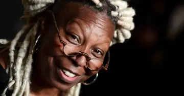 Uśmiechnięta Whoopi Goldberg w okularach i z dredami. Ikona kina, znana z wielu filmów, seriali i programów.